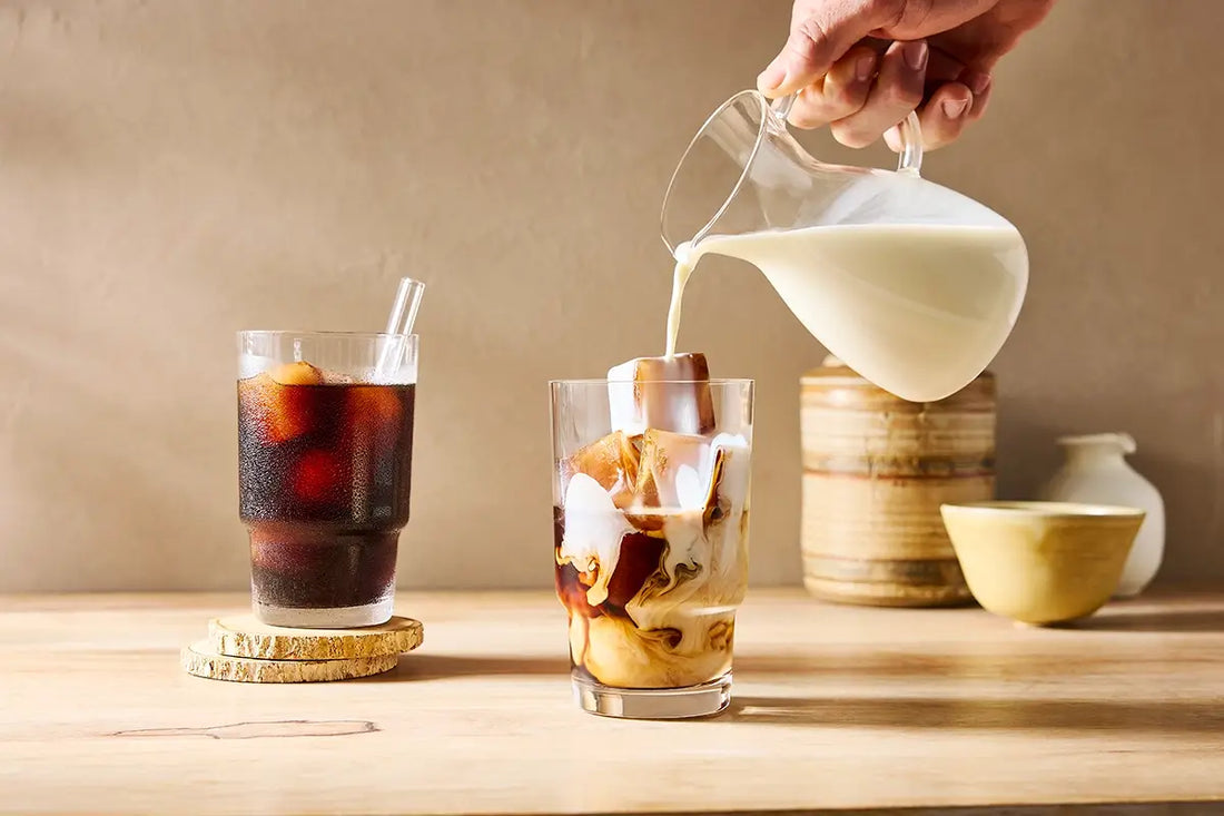 pouring cream into coffee with iced coffee cubes