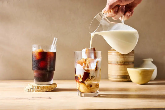 pouring cream into coffee with iced coffee cubes