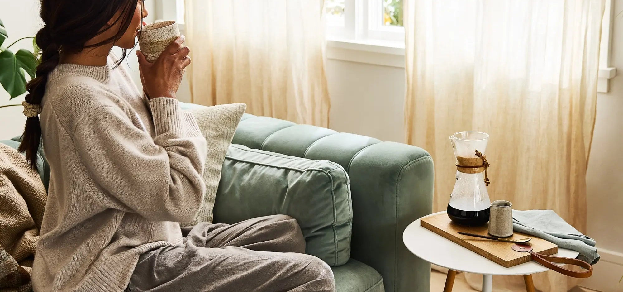 Woman sitting on a couch drinking coffee in a cozy living room.